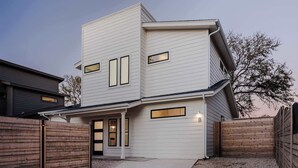 Een modern huis met twee verdiepingen, een plat dak, een veranda en een houten omheining.