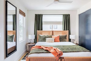 Une chambre d’hôtel comprenant un lit, deux tables de chevet, un miroir, un ventilateur de plafond et une fenêtre avec des rideaux.