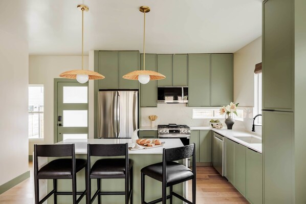 Una cocina moderna con gabinetes verdes, una isla central con sillas, una estufa y luces colgantes.
