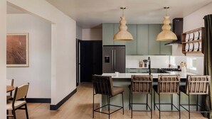 A modern kitchen with a central island, bar stools, pendant lighting, and a dining area with a table and chairs.