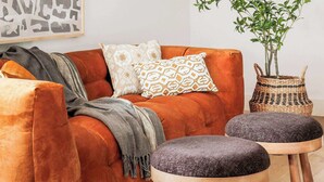 A living room with a red sofa, two grey ottomans, a woven basket, and a potted plant.