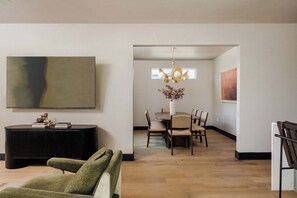 A modern living room with a sofa, a dining area with a table and chairs, and a hallway leading to another room.