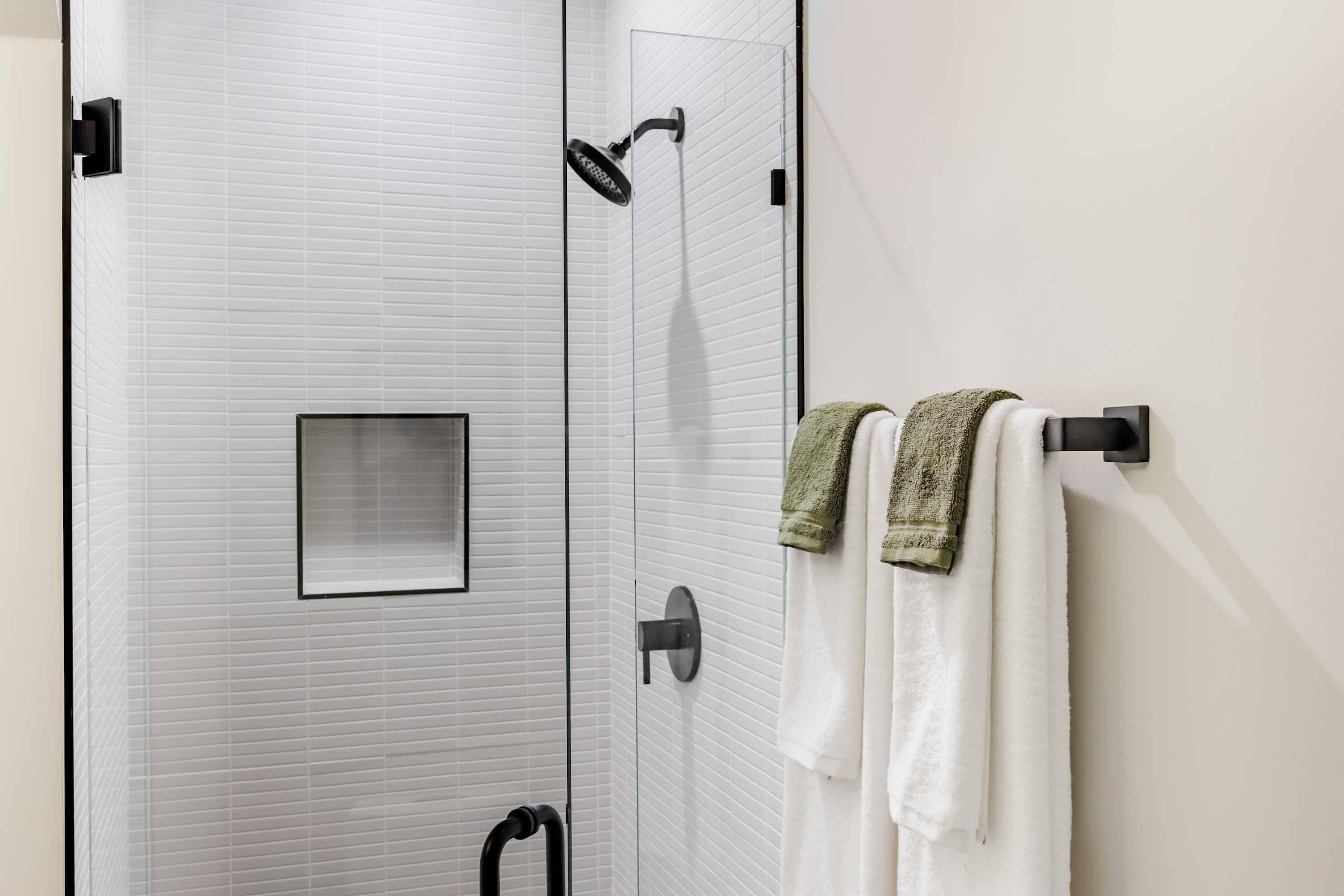 A bathroom with a white tiled wall, a glass shower enclosure, and two towels hanging on a towel rack.