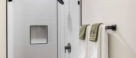 A bathroom with a white tiled wall, a glass shower enclosure, and two towels hanging on a towel rack.