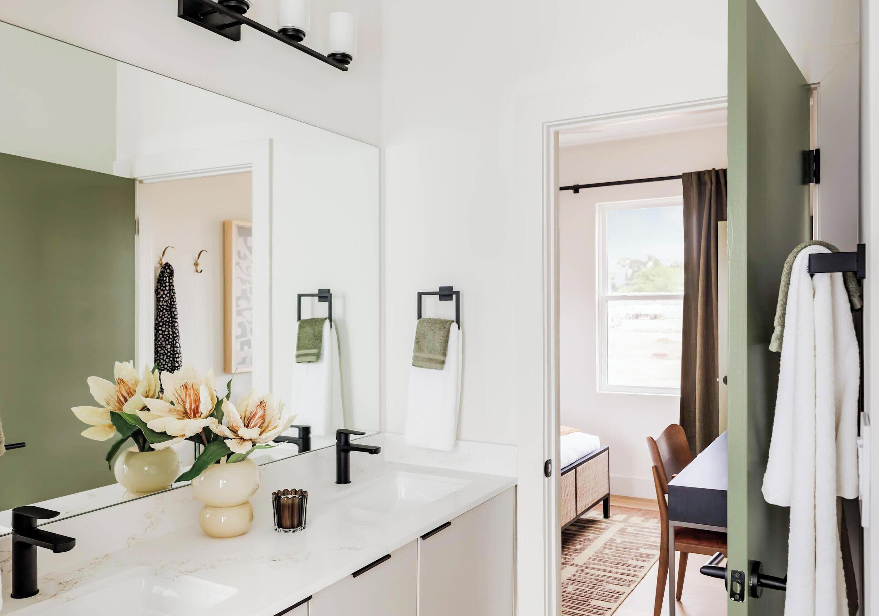 Un baño moderno con un espejo grande, tocador blanco y zona de ducha visible a través de una puerta abierta.