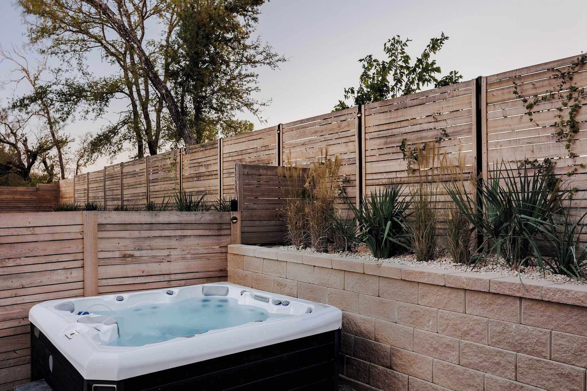 A hot tub in a landscaped outdoor area with a wooden fence and plants.