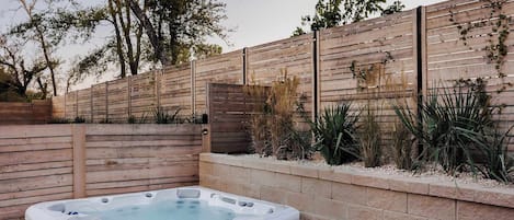 A hot tub in a landscaped outdoor area with a wooden fence and plants.