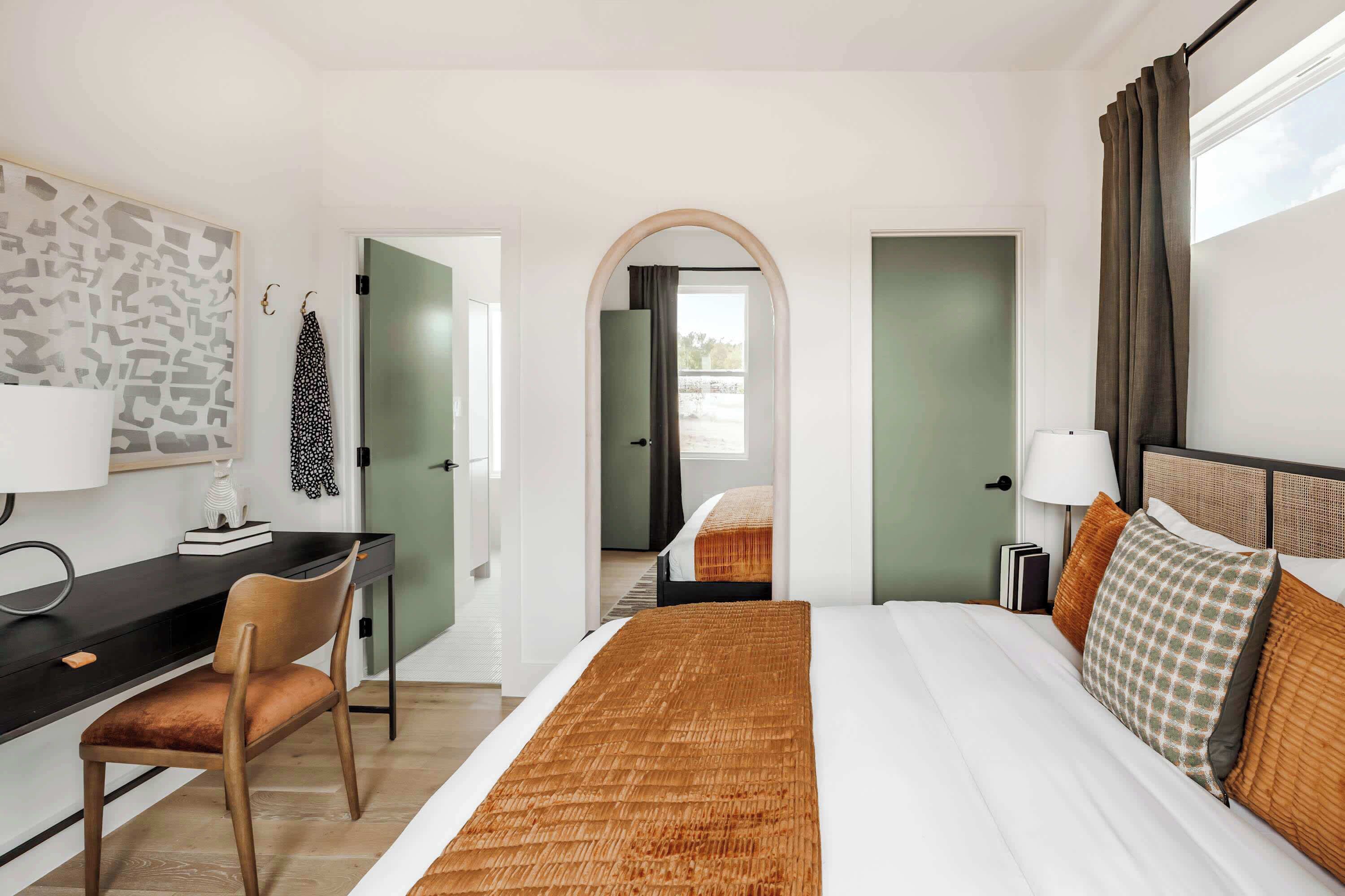 A hotel room with a bed, desk, chair, and a view through an arched doorway.