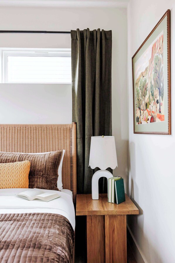 A hotel room with a bed, a nightstand with books, a lamp, and a painting on the wall.