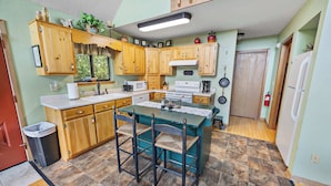 A kitchen with wooden cabinets, a central island with bar stools, a microwave, stove, and a sink. - Above It All Cabin - Mountain Views (Murphy)