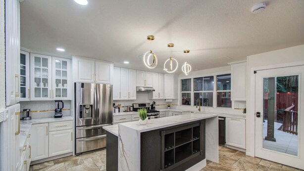 A modern kitchen with white cabinetry, stainless steel appliances, a central island, and a large window providing natural light. - 5BD/3BA Stylish Home w Game Room, Backyard, Pool (Spring)