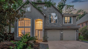 A two-story house with a stone facade, large windows, and a garage. - 5BD/3BA Stylish Home w Game Room, Backyard, Pool (Spring)