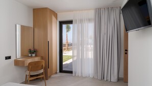 A modern hotel room with a bed, a desk with a chair, a TV, and a large window with curtains. - Divel Luxury Villas - Villa Ervin by Estia (Hersonissos)