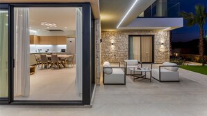 A modern house with a stone exterior, a dining area with a table and chairs, and an outdoor seating area with sofas and a coffee table. - Divel Luxury Villas - Villa Ervin by Estia (Hersonissos)