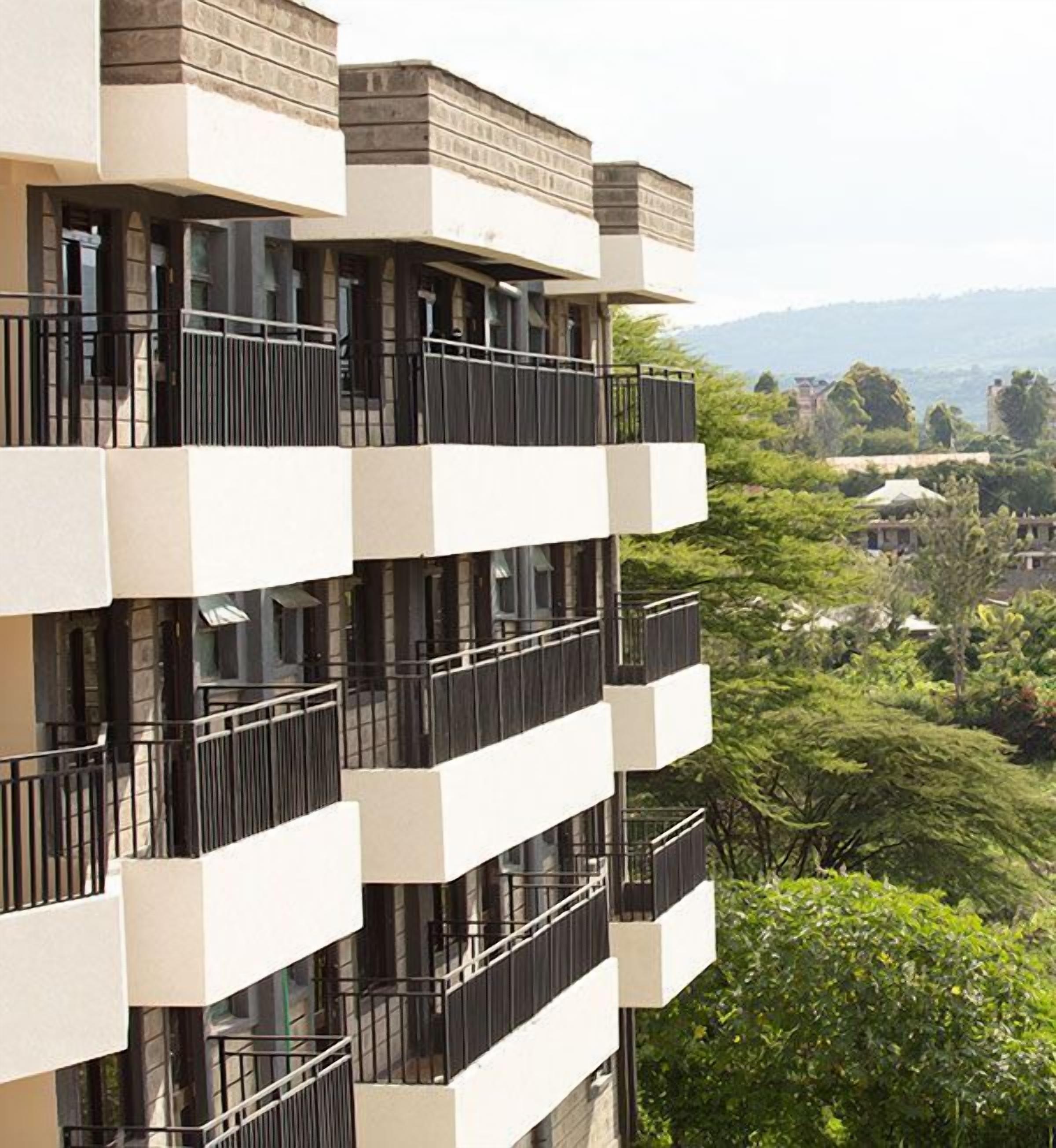 Un edificio de varios pisos con balcones, vistas a zonas verdes y colinas al lejano.
