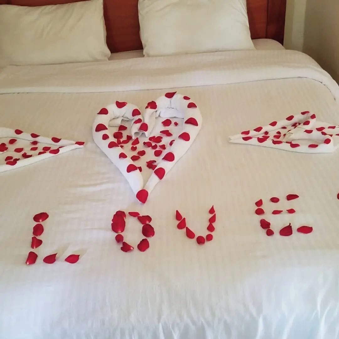 Una cama con un arreglo de pétalos de rosa en forma de corazón que deletrea 'LOVE' sobre la colcha.
