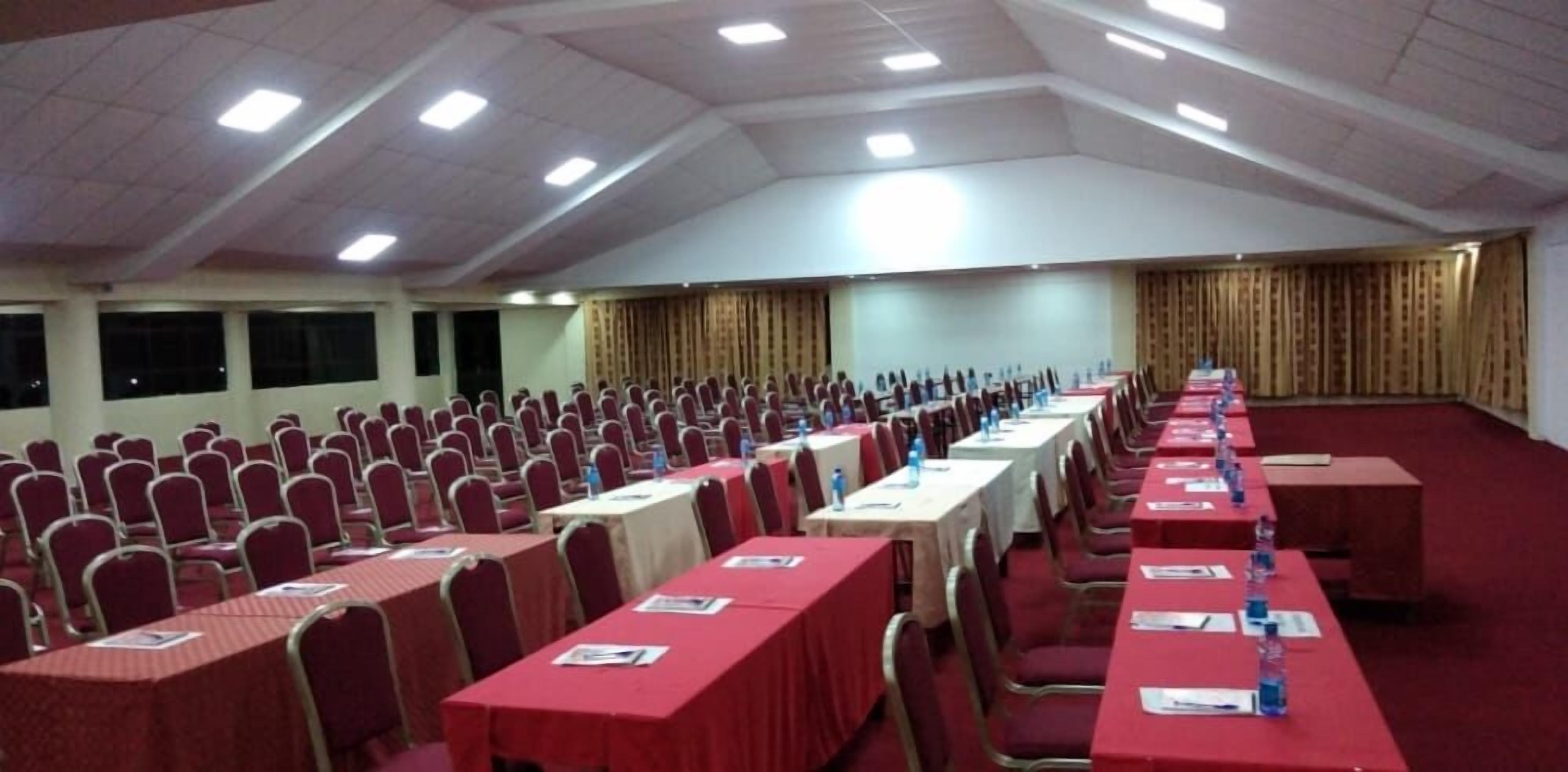 Un amplio salón de conferencias con filas de sillas y mesas rojas, equipado con botellas de agua y tarjetas de identificación.