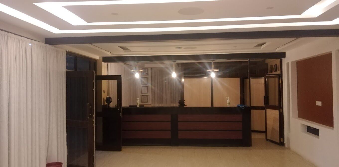 A hotel lobby with a reception desk, a wooden counter, and a modern ceiling design.