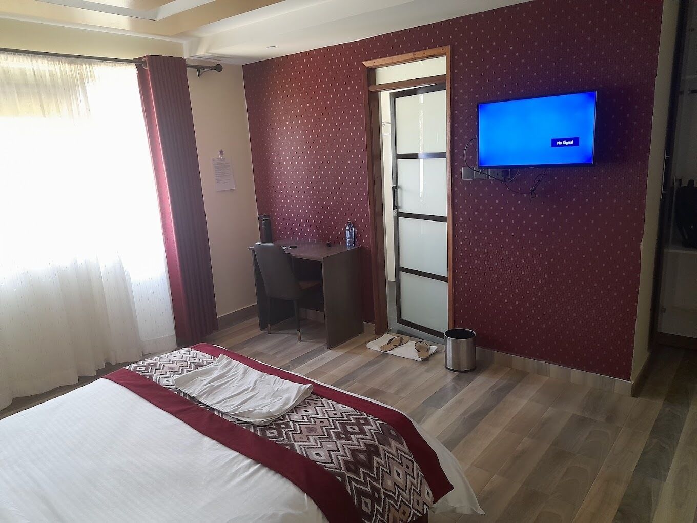 A hotel room with a bed, a desk, a chair, a television, and a door.