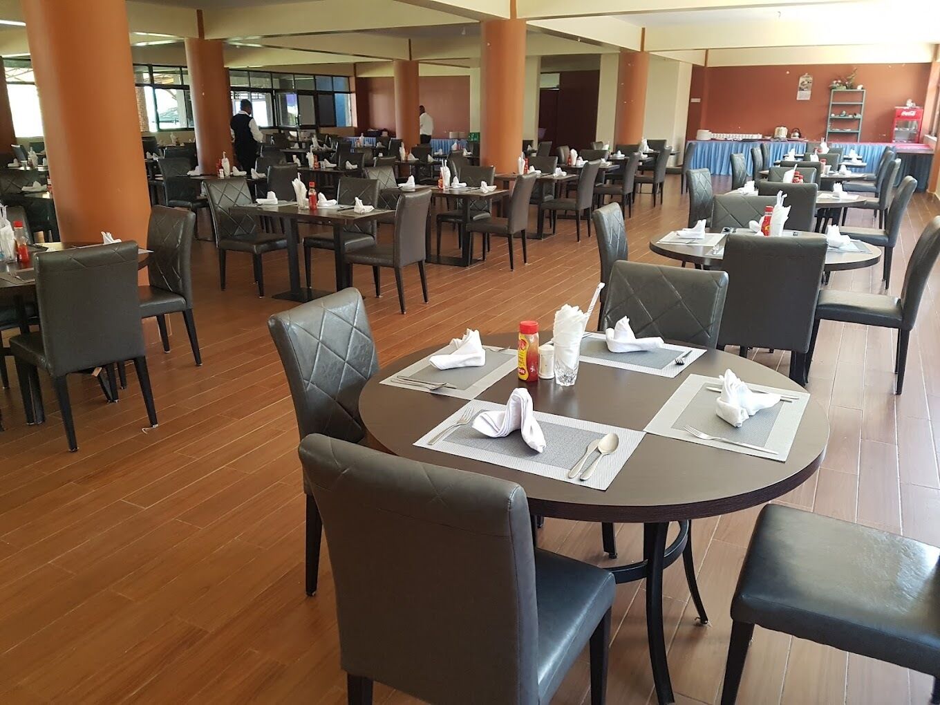 Un comedor espacioso con varias mesas y sillas, ventanas amplias y un diseño moderno y limpio.