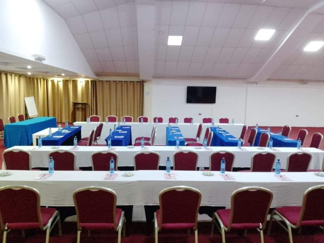 A conference room with rows of tables and chairs, a podium, and a television screen on the wall.