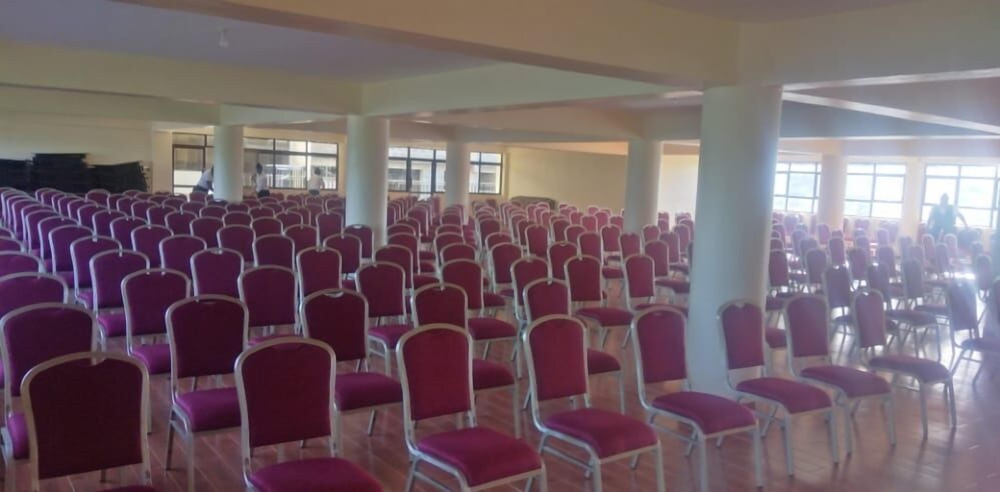 A large hall with rows of red chairs and white tables, likely for events or meetings.