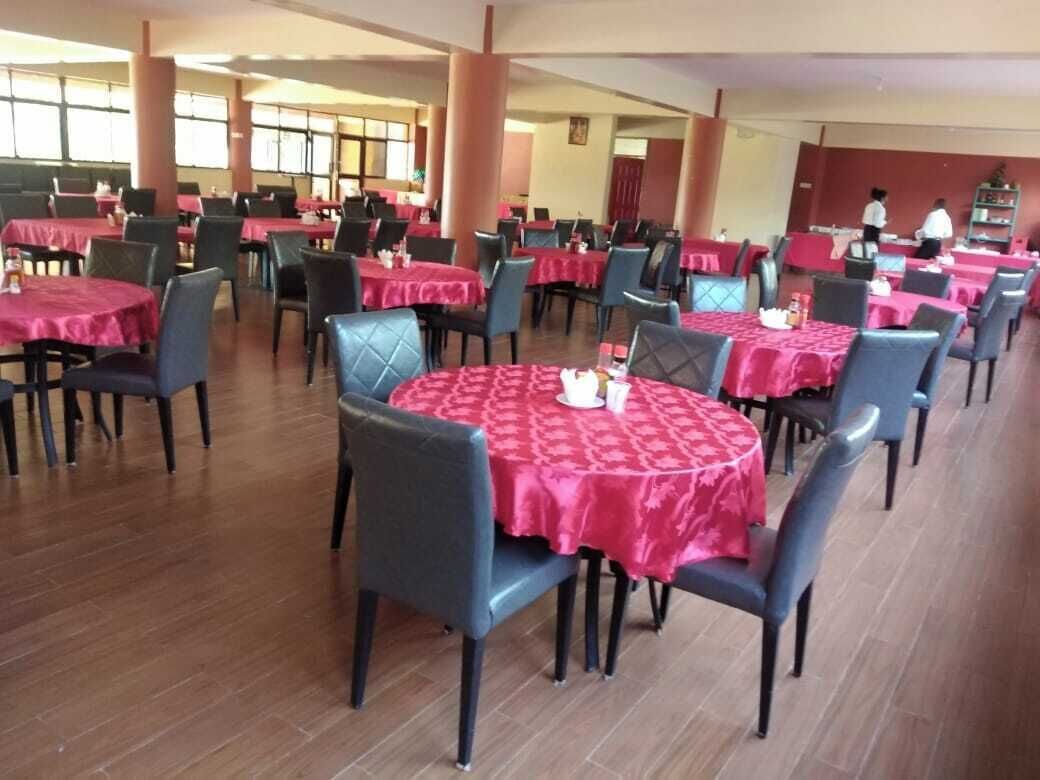 Uma área de refeições com mesas redondas cobertas por toalhas vermelhas, dispostas em fileiras com cadeiras.