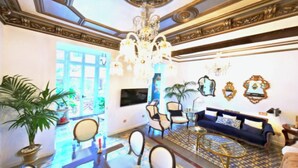 A spacious lobby with a chandelier, sofas, chairs, and a TV.