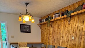 A dining area with a wooden table, chairs, a woven rug, and a wooden wall with shelves.