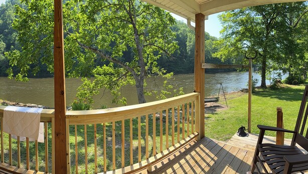 A covered porch with a view of a river and forest.
