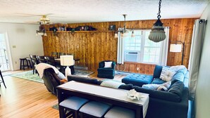 A living room with a wooden wall, a blue sofa, a dining table with chairs, and a ceiling fan.