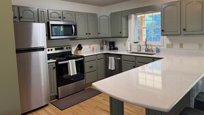 A modern kitchen with stainless steel appliances, light green cabinets, and a large window providing natural light.