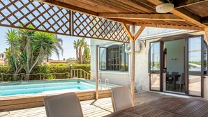 A wooden deck with a pool, outdoor seating, and a covered area with a lattice ceiling.