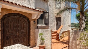 A stone building with a large wooden door, a small potted plant, and a staircase leading to an upper level.