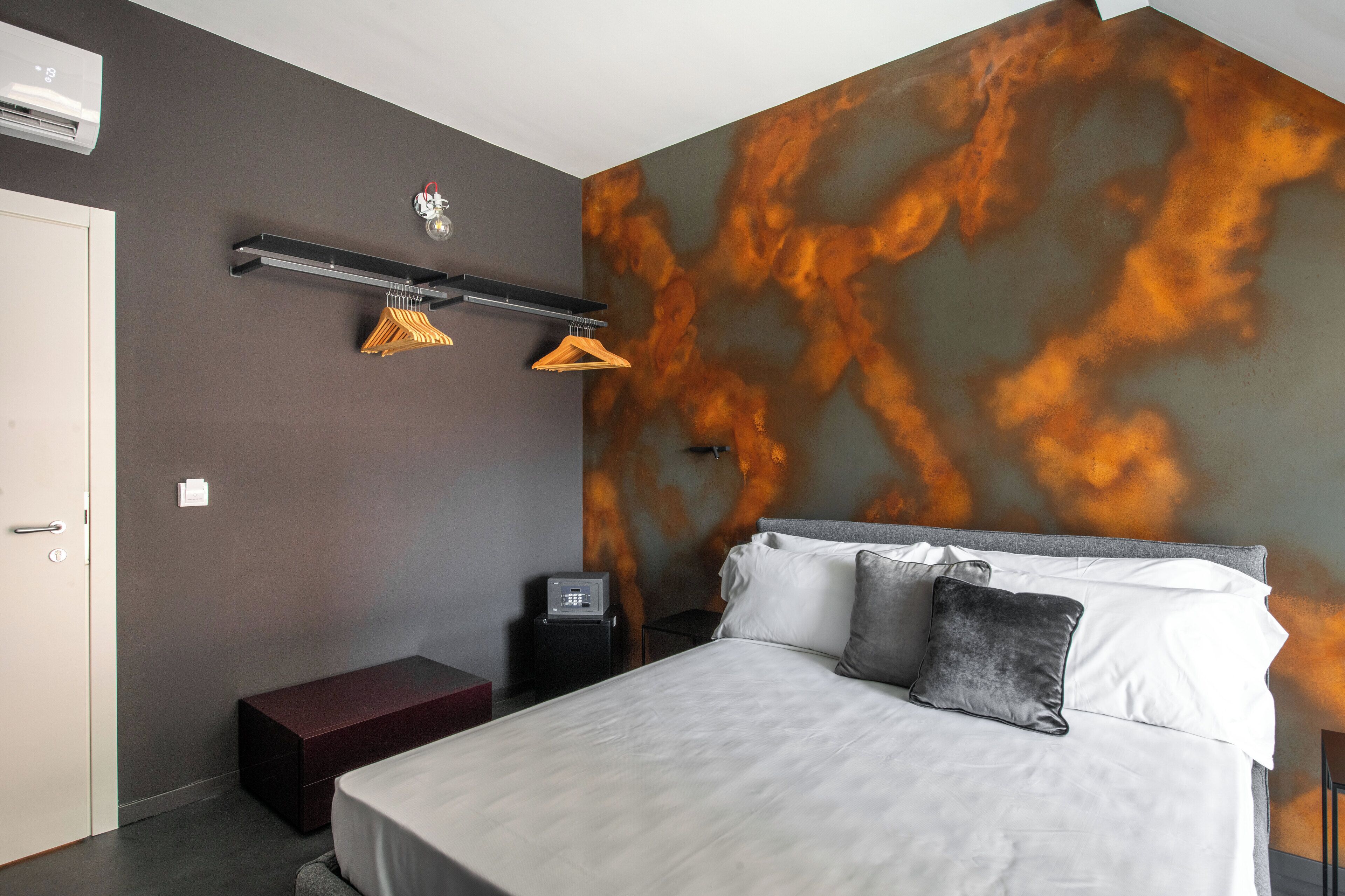 Une chambre d’hôtel moderne dotée d’un grand lit, d’une armoire, d’une table de chevet et d’un mur orné d’un motif abstrait original aux couleurs orange et grise.