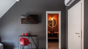 Moderni huone, jossa on seinälle asennettu taulutelevisio, pieni pöytä ja punainen tuoli sekä ovi, joka johtaa keittiötilaan.
