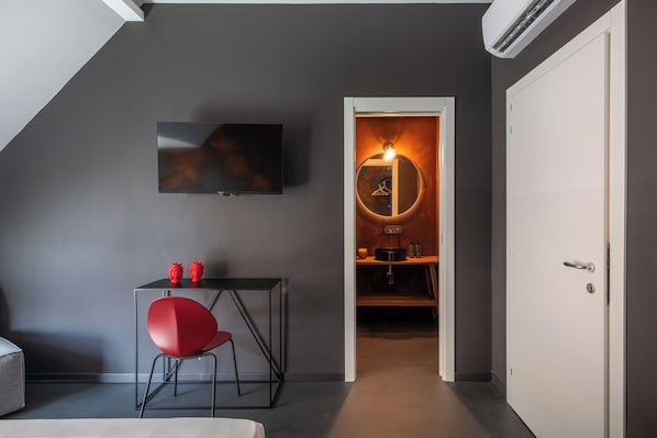 A modern room with a flat-screen TV mounted on the wall, a small table with a red chair, and a doorway leading to a kitchen area. - Massimo Foyer 53 by Wonderful Italy (Palermo)