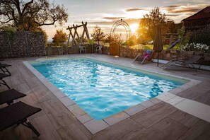 A rectangular swimming pool with a stone border, surrounded by lounge chairs and a wooden deck. - Apartment 'Rose' with Mountain View, Shared Pool and Wi-Fi (Freiamt)
