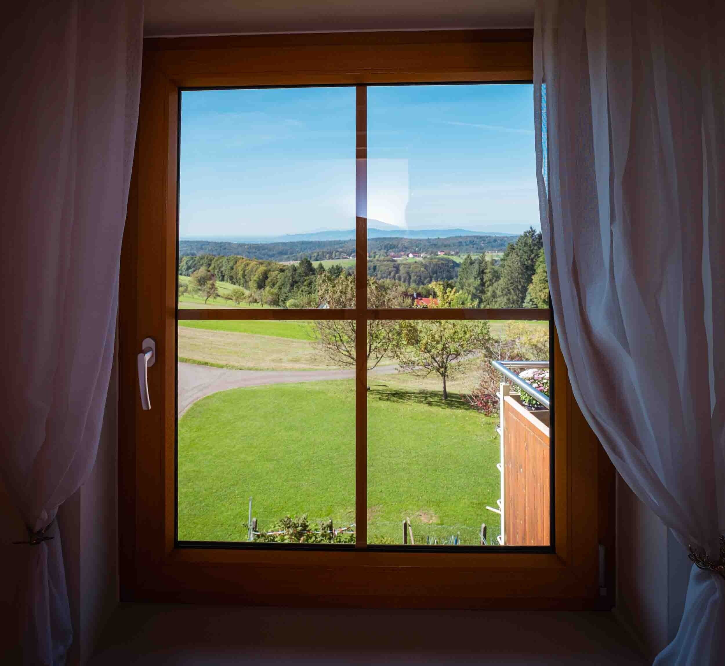 A room with a large window, curtains, and a view of a green landscape.