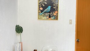 Ein kleiner Essbereich mit einem Holztisch, zwei weißen Plastikstühlen, einem Topfpflanzen und einem Bilderrahmen mit einem Vogelmotiv an der Wand.