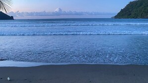 Ein Strand mit ruhigen Wellen, blauem Himmel und einem entfernten Berg.