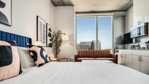 Een moderne hotelkamer met een groot bed, een zithoek, een kitchenette en uitzicht op de skyline.