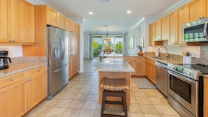 A modern kitchen with wooden cabinets, stainless steel appliances, and a central island. - Nihilani 18C Newly renovated plantation style home (Princeville)