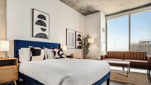 A modern hotel room with a large bed, a sofa, a desk, and a large window offering a city view. - Boulevard Stays Highrise STU Sky Pool, Parking, Gym 26 (Phoenix)