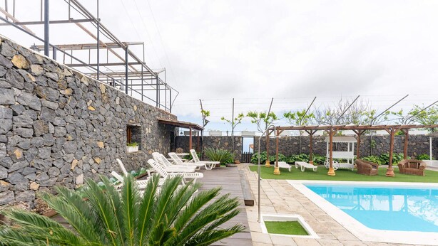 Ein Poolbereich mit Steinmauer, Liegestühlen und einer Pergola.