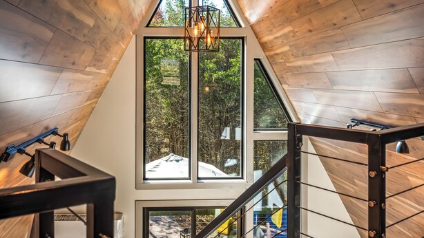Un intérieur moderne avec un plafond en pente en bois, de grandes fenêtres et un luminaire central.