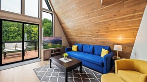 Un salon moderne avec un canapé bleu, un fauteuil jaune et un téléviseur fixé sur un mur en bois.