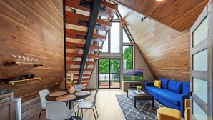 Une pièce chaleureuse de style loft, avec un intérieur en bois, un coin repas comprenant une table ronde et des chaises, un canapé bleu et un escalier menant à un niveau supérieur.