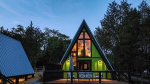Une cabane moderne de forme triangulaire, dotée d’une terrasse et d’un escalier menant à l’entrée.