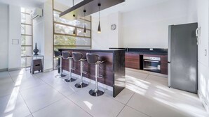 Cozinha moderna com área de bar, eletrodomésticos de aço inoxidável e uma grande janela que oferece muita luz natural.